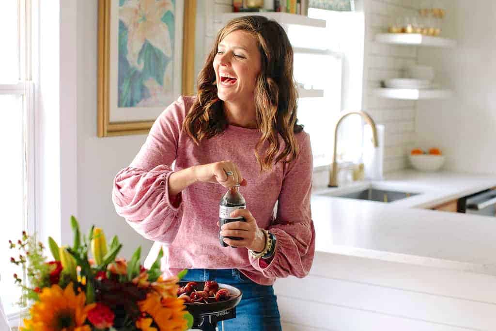 woman with a pink top sitting at table drinking a soda laughing
