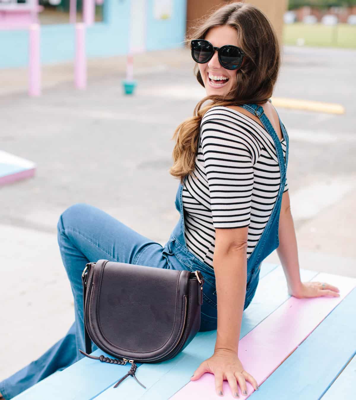 woman sitting on a picnic table in overalls with sunglasses on