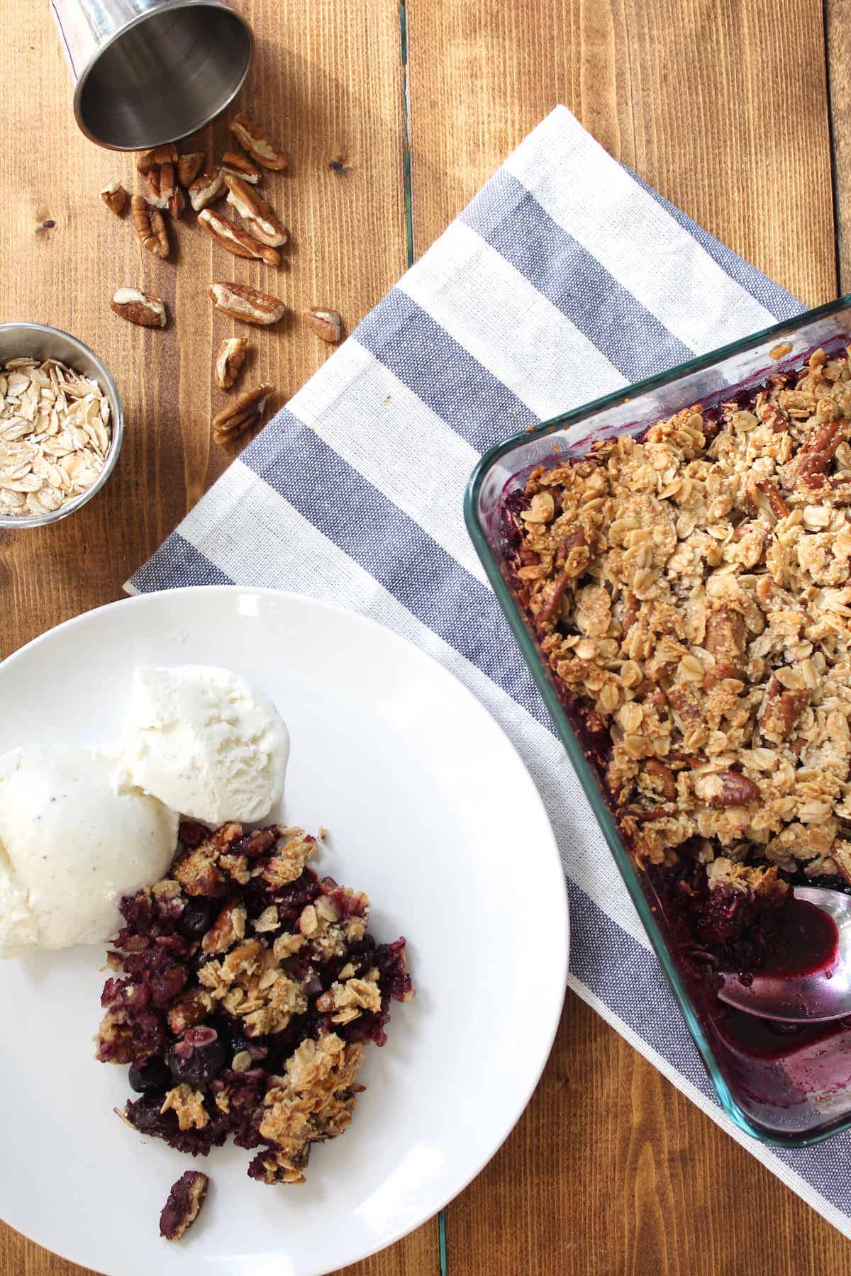 shot from above of a table a dish of berry crisp and a plate with a serving of the crips with vanilla ice cream and pecans