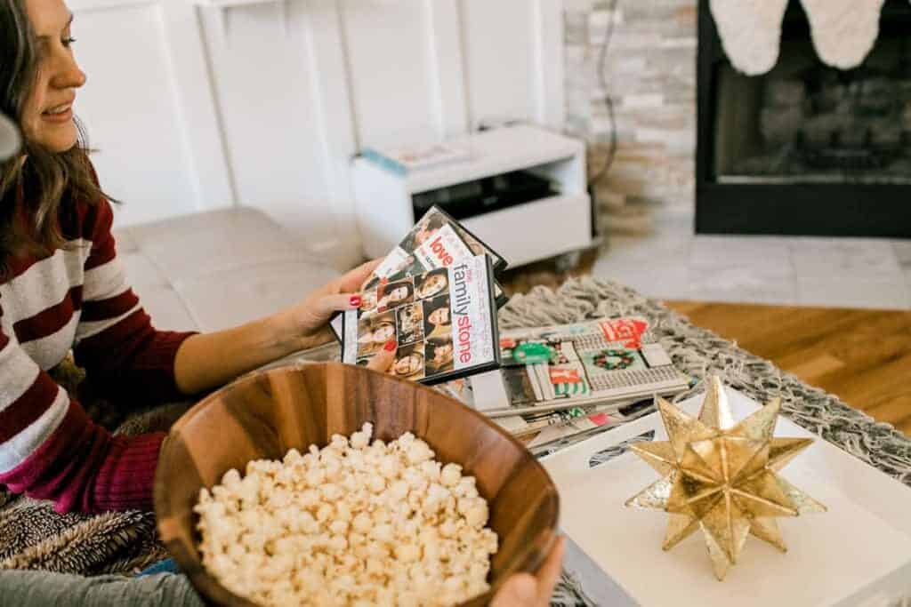 How to Host a Christmas Movie Marathon & Cookie Swap. Woman holding several DVD's and a large bowl of popcorn.