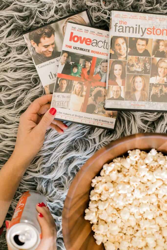 How to Host a Christmas Movie Marathon & Cookie Swap. Image of hand holding three dvd's and a bowl of popcorn from above.