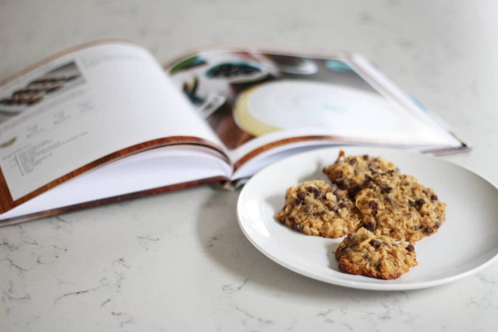How to Host a Christmas Movie Marathon & Cookie Swap. Image of a plate of cookies next to an open book on a countertop.
