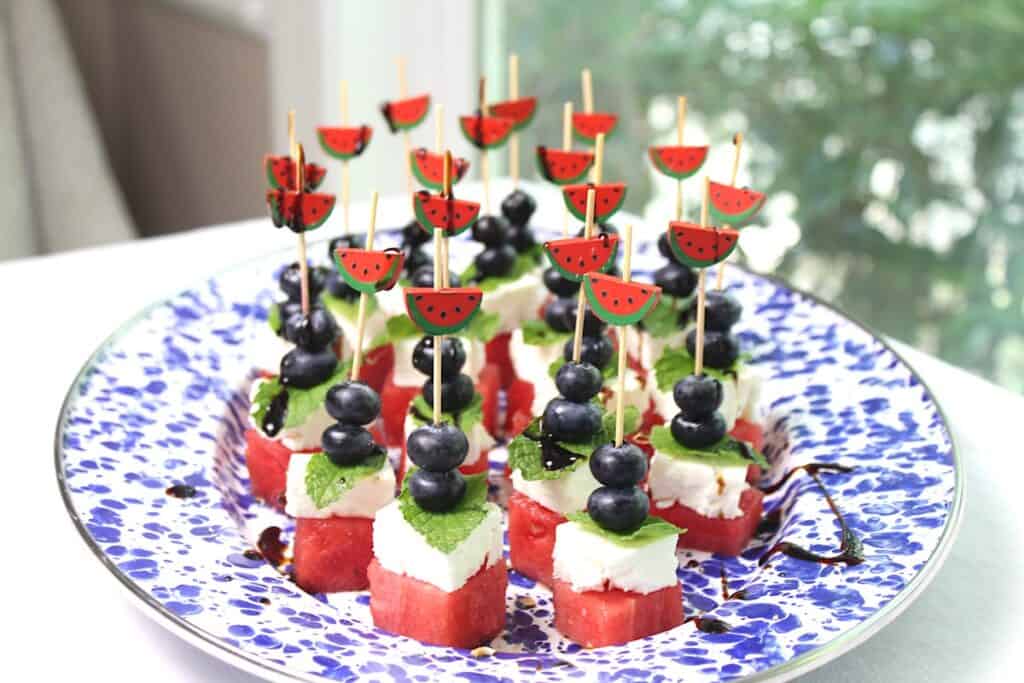 Watermelon Skewers with Feta, Mint and Blueberries with watermelon skewers on a blue speckled platter.