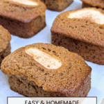 Golden brown mini bread loaves on parchment paper, featuring a single baked apple slice on each one.