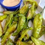 air fried shishito peppers with creamy dipping sauce on a white platter.