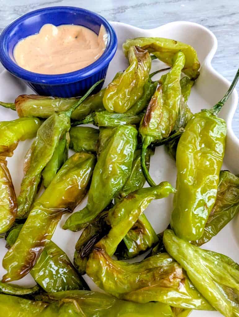 air fried shishito peppers with creamy dipping sauce on a white platter.