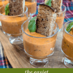 Individual servings of creamy tomato basil bisque with goat cheese, presented in mini dessert glasses with a grilled cheese toast point.