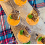 overhead shot of creamy tomato soup appetizers, topped with a fresh basil leaf and a slice of a grilled cheese sandwich