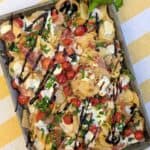 A trendy viral "chipcuterie" board, featuring a sheet pan of potato chips loaded with caprese-inspired toppings like fresh mozzarella, cherry tomatoes, and basil, and finished with a rich balsamic glaze.