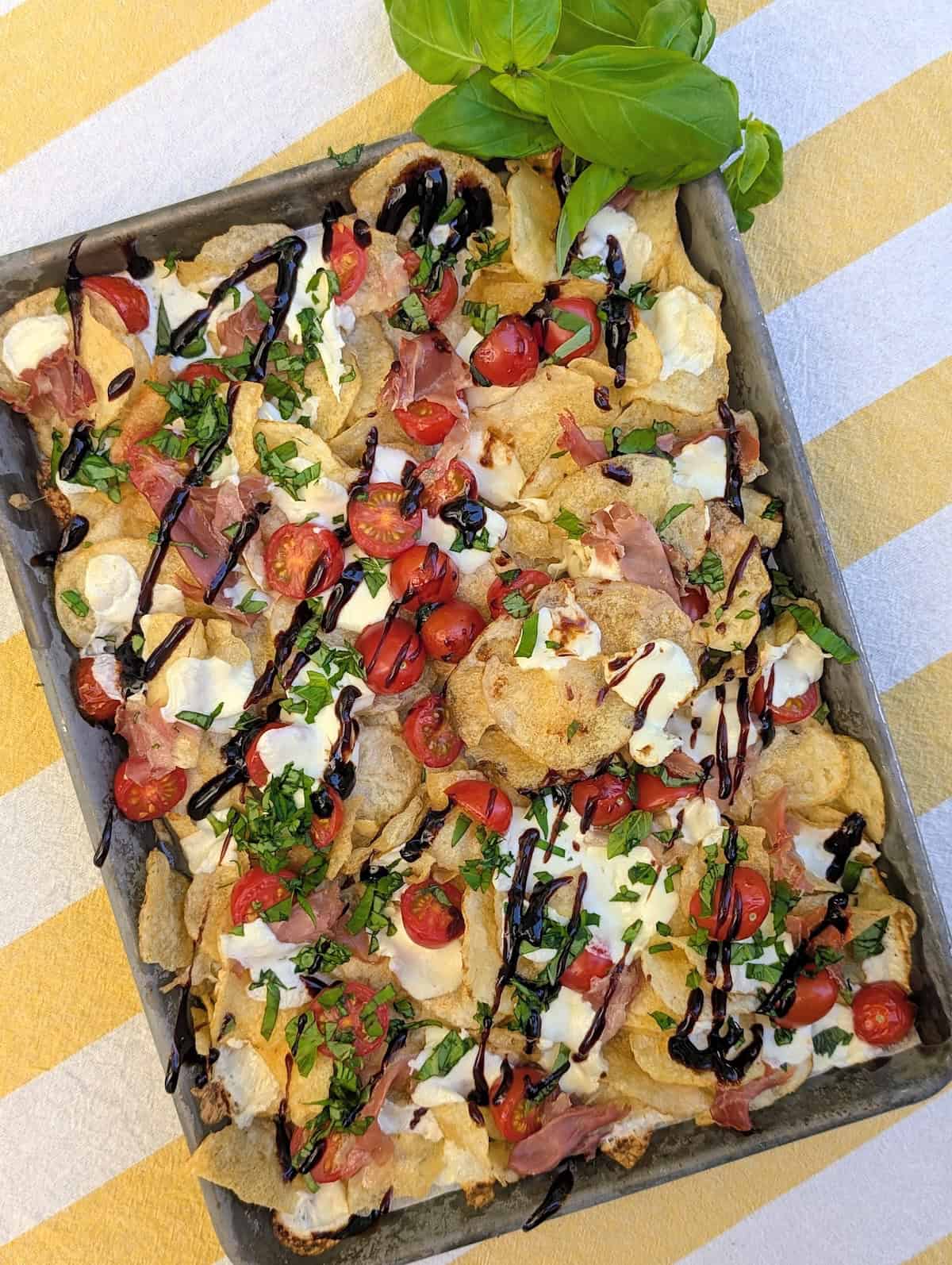 A trendy viral "chipcuterie" board, featuring a sheet pan of potato chips loaded with caprese-inspired toppings like fresh mozzarella, cherry tomatoes, and basil, and finished with a rich balsamic glaze.