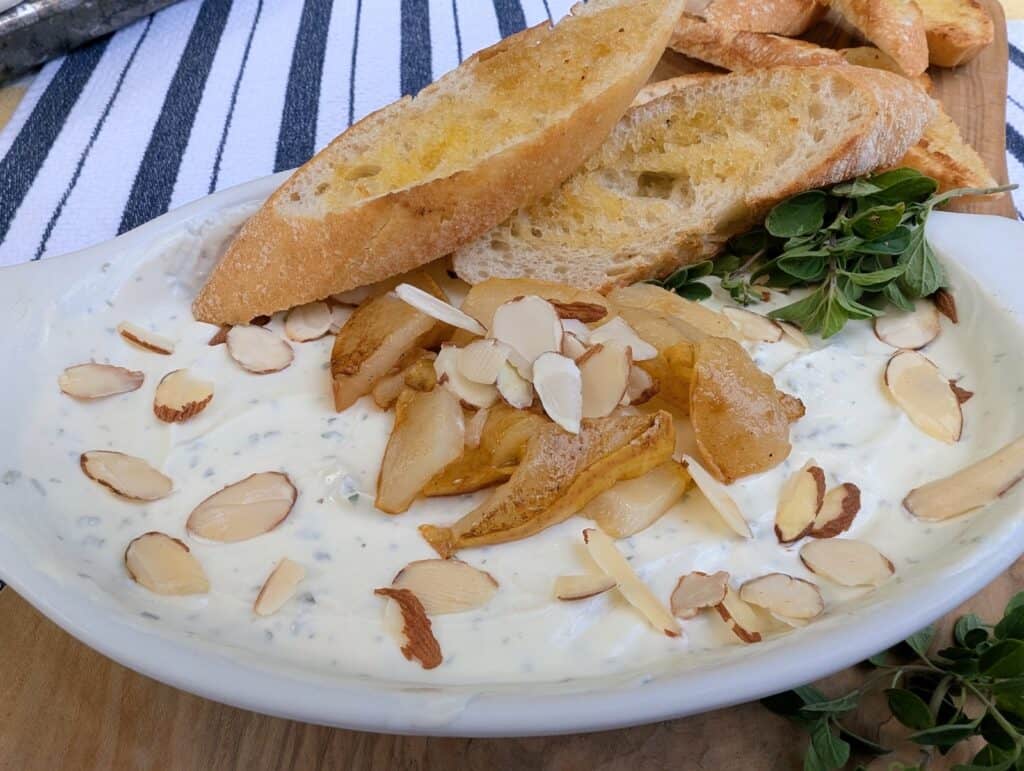 Creamy Whipped Goat Cheese Dip with Honey and Herbs in a white serving bowl topped with sliced almonds and grilled pears with crusty bread