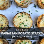 Overhead photo of several baked Parmesan Potato Stacks, sprinkled with fresh parsley and resting on white parchment paper. Text overlay reads: "The Best Parmesan Potato Stacks {in muffin tins}."