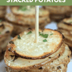 An extreme close-up of a single serving of a baked, garlic and parmesan stacked potato, secured with a small wooden skewer. The top layer is golden and crispy. Text overlay reads: "the ultimate Garlic & Parmesan Stacked Potatoes."
