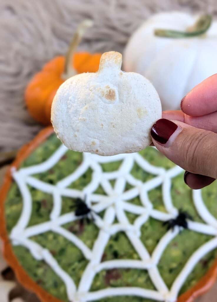 hand holding a pumpkin chip of The Ultimate Halloween Guacamole with Spooky Chips