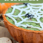A close, low-angle shot of the Halloween Guacamole Dip in an orange pumpkin-shaped bowl, featuring the creamy white spider web design. Cutout tortilla chips are piled in the foreground. Text overlay reads: "the ultimate Halloween Guacamole Dip & Spooky Chips."