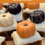 Close-up shot of individual pumpkin spice cake bites, cut from a Trader Joe's Mini Sheet Cake, topped with white frosting and assorted chocolate pumpkin candies. Text overlay reads: "the easiest Trader Joe's Mini Sheet Cake Hack."