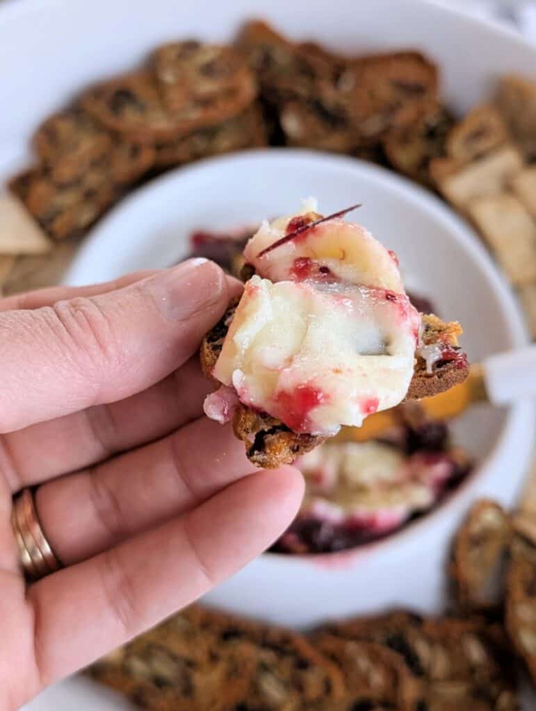 hand holding a cracker with Baked Brie with Cranberry Sauce and Pistachios