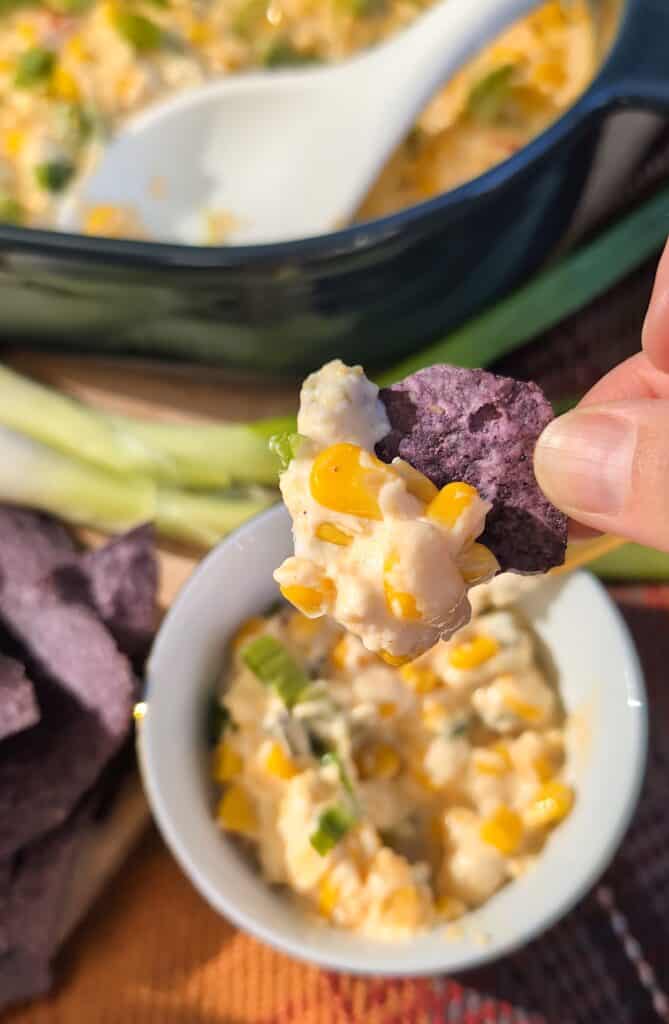 overhead shot of a hand holding a chip with a scoop of creamed corn dip