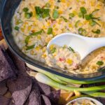 Baked Creamed Corn Dip with spoon scooping out a serving with chips.