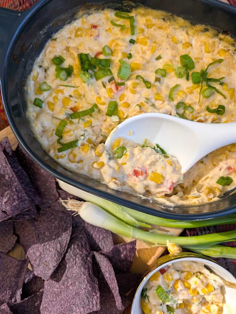 Baked Creamed Corn Dip with spoon scooping out a serving with chips.