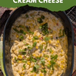 An overhead view of a hot, creamy corn dip with bits of red pepper, topped generously with chopped green onions, served in a dark blue oval baking dish. Text overlay reads: "easy & delicious Hot Corn Dip with Cream Cheese."