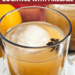 Close-up of a single cocktail glass holding spiced apple cider over a large spherical ice cube, garnished with a star anise. Text overlay reads: "the ultimate Spiked Apple Cider Cocktail with Fireball."