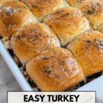 Tilted view of a white baking dish containing twelve shiny, baked King's Hawaiian rolls topped with a buttery glaze and poppy seeds, revealing the turkey and cranberry filling underneath. The text on the image reads "EASY TURKEY CRANBERRY SLIDERS, THANKSGIVING LEFTOVERS."