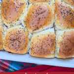 Close-up overhead photo of a tray of twelve baked, golden-brown King's Hawaiian sweet rolls sprinkled with poppy seeds, filled with turkey and cranberry sauce, ready to be pulled apart into sliders.