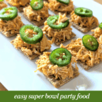 Buffalo chicken dip bites served on crackers and topped with sliced jalapeños on a white platter.
