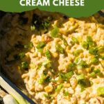 Hot corn dip with cream cheese baked in a glass dish and topped with sliced green onions, served with tortilla chips.