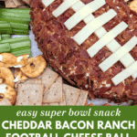 Cheddar bacon ranch football-shaped cheese ball decorated with cheese strips and surrounded by crackers and vegetables.