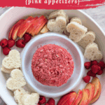 Overhead view of a strawberry dessert cheese ball coated in crushed freeze-dried strawberries surrounded by apple slices and heart-shaped bread.