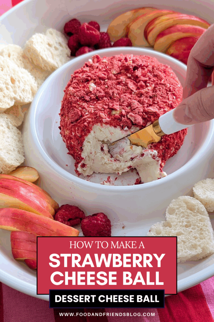Hand slicing into a strawberry cheese ball coated in freeze-dried strawberries on a white serving platter.