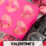 Heart-shaped ice cubes in a pink silicone mold with prosecco bottle and dried pink roses on a Valentine’s-themed background.