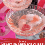 Close-up of a coupe glass with a heart-shaped ice cube melting in a pink sparkling drink.