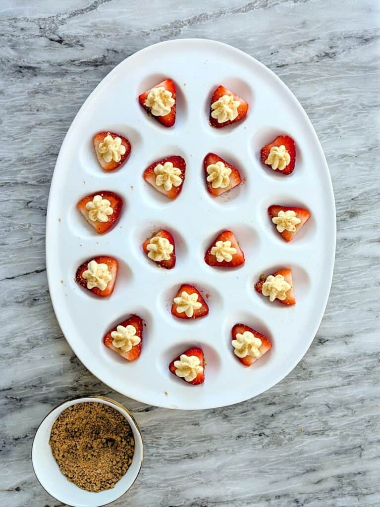 The Easiest Cheesecake Deviled Strawberries Recipe over head with small bowl of graham cracker crumbs