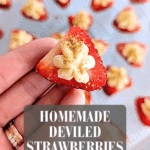 Hand holding a deviled strawberry filled with cream cheese frosting and sprinkled with graham cracker crumbs.